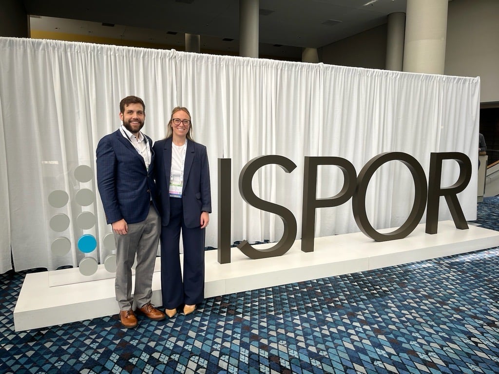 CPS team members Drs. Giavatto and Wash stand in front of the ISPOR 2024 sign as they attend and present at the conference.